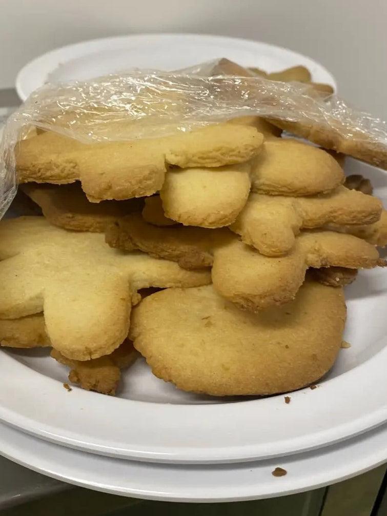 A pile of gingerbread-shaped sugar cookies, lightly golden and wrapped in plastic, resting on a white plate.
