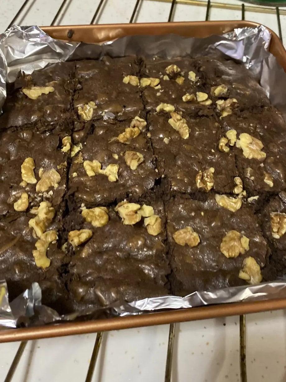 A tray of chocolate brownies topped with walnut pieces, cut into squares and lined with aluminum foil.