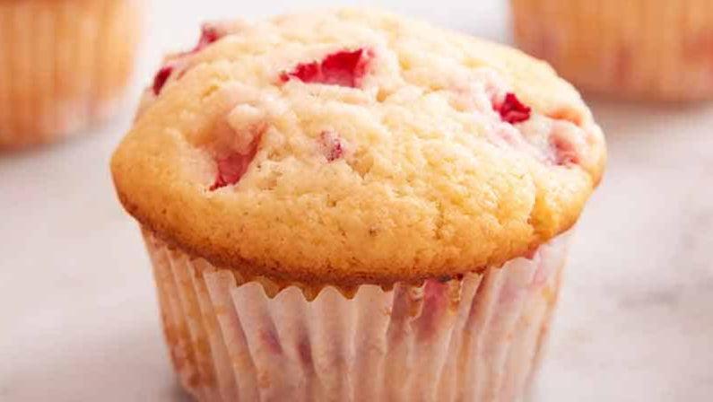 Close-up of a freshly baked strawberry muffin with a light golden-brown top and visible red strawberry bits.