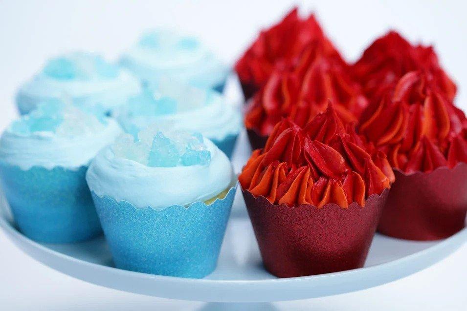 A plate with four blue cupcakes topped with clear crystals and four red cupcakes with swirled red frosting, arranged in two rows.