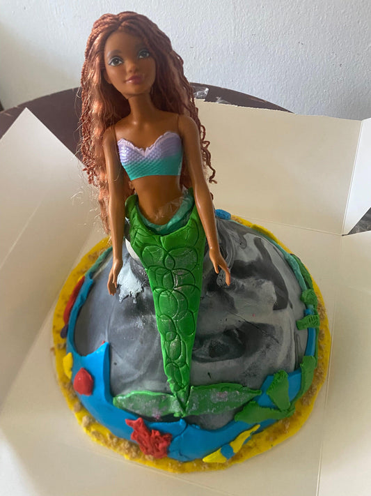 A merma decorates a cake designed like an underwater scene, featuring colorful icing and ocean-themed details.