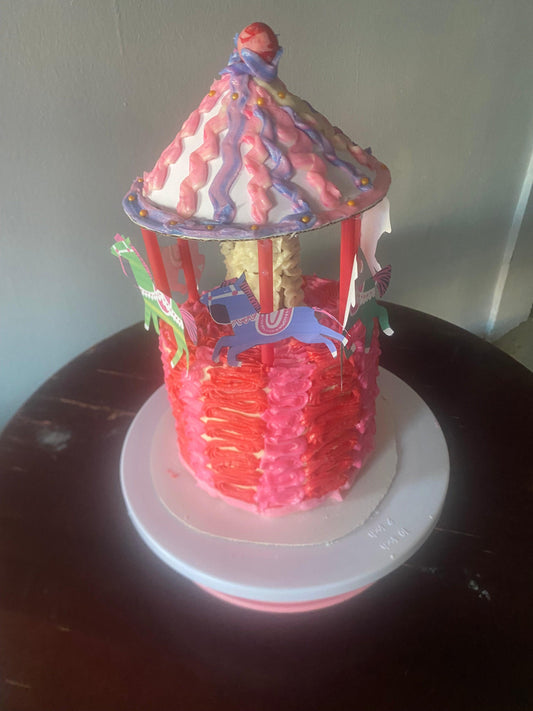 A colorful cake shaped like a gazebo, decorated with pink icing and horses, sitting on a white cake board.